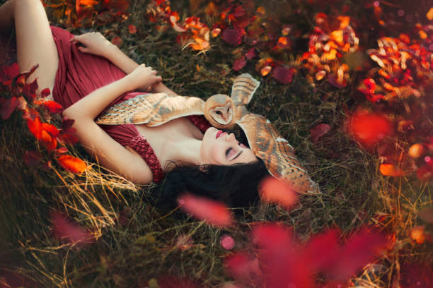Falling deeply Los Angeles-bright photo in burgundy shades, girl in dark dress color of Marsala, lady with dark hair lies on grass, fallen red and yellow leaves, barn owl spread its wings on sleeping fairy and protects sleep.