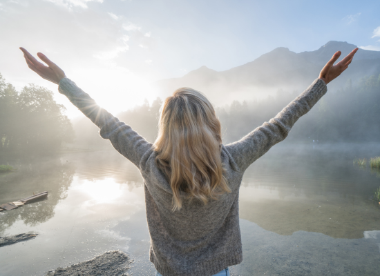 Blonde-haired woman with arms outstretched, standing confidently against a bright background, symbolizing empowerment and celebration during Women’s History Month.